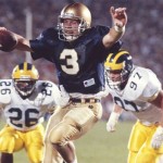 Notre Dame quarterback Rick Mirer scores a touchdown against the defense of Michigan's David Key (26) and Chris Hutchinson (97) at Notre Dame Stadium on Sept. 15, 1990. (Getty Images / John Biever)